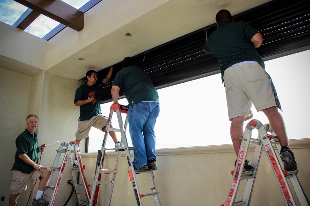 Workers installing window blinds on ladders
